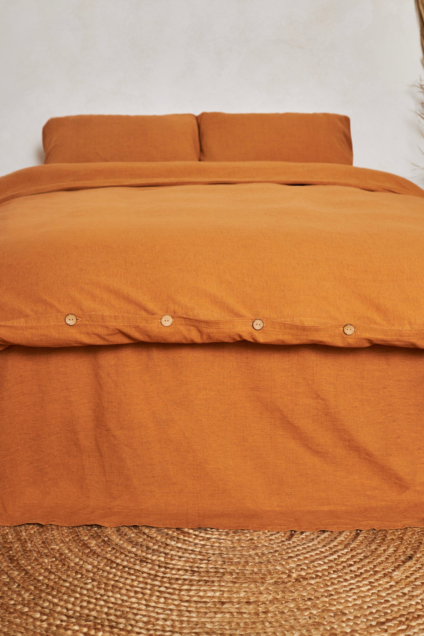 Cinnamon orange linen duvet cover set with buttons placed on a bed against a white wall.