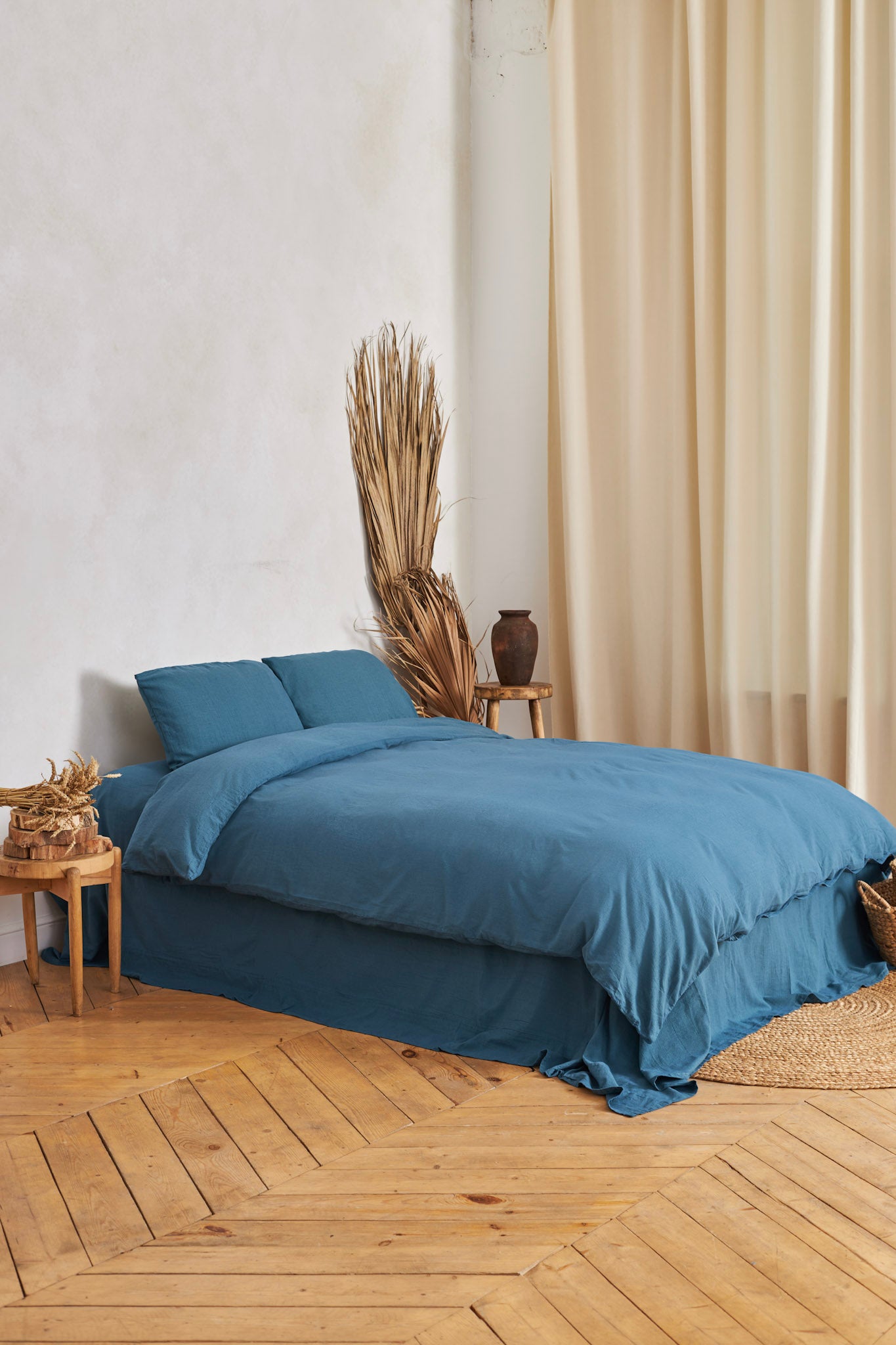 Blue linen duvet cover set on a bed in a room with wooden flooring and beige curtains.