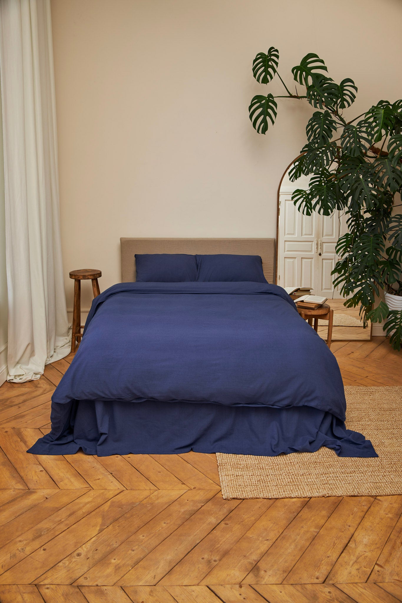 Dark blue linen duvet cover set on a bed in a room with wooden flooring and a plant.