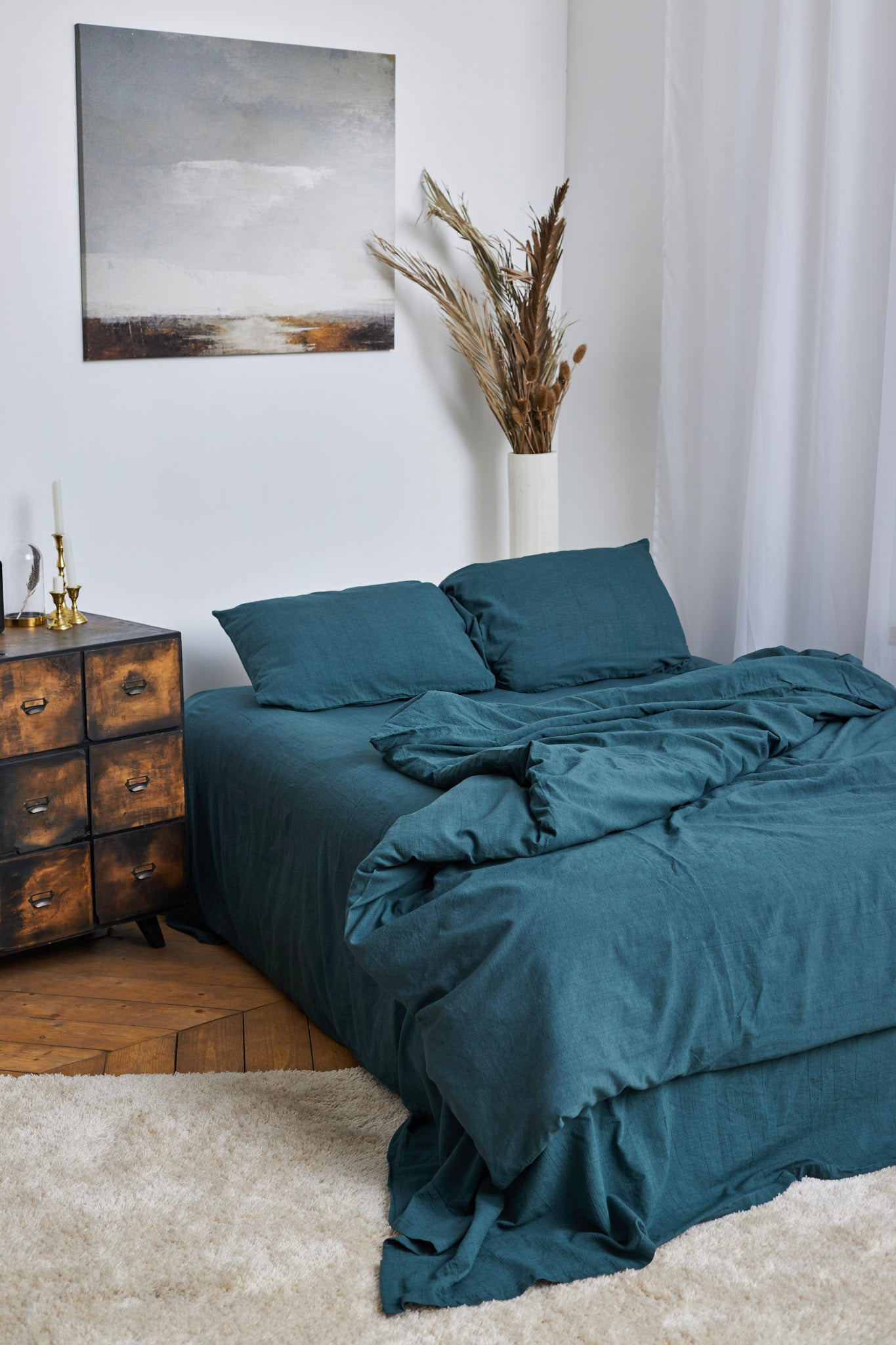 Blue green washed linen bedding set on a bed in a bedroom with a wooden dresser and decorative items.
