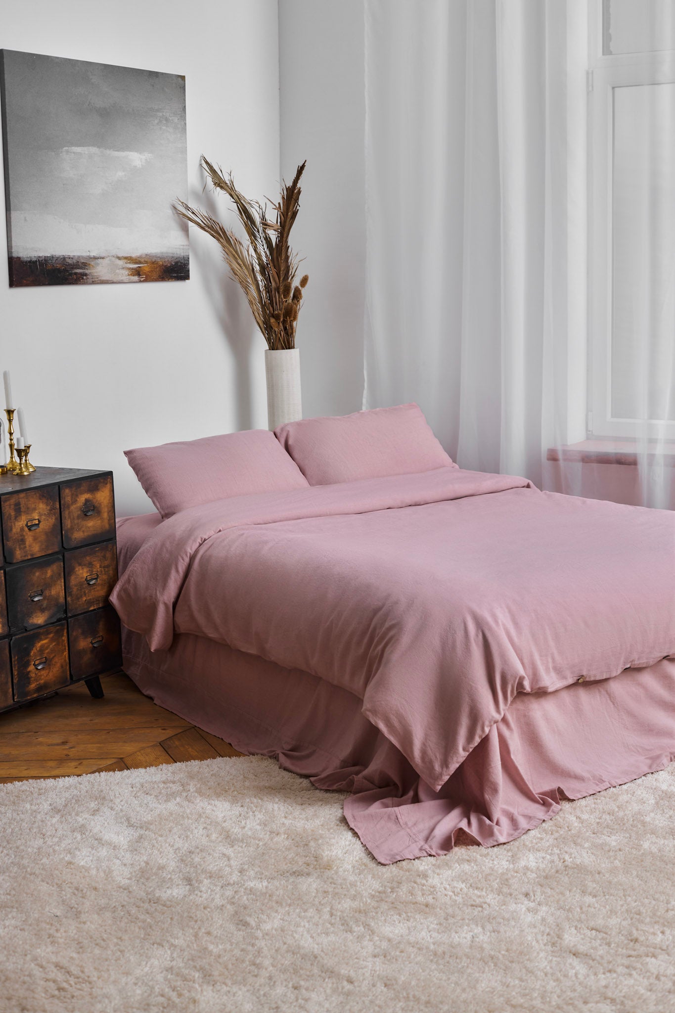 Pink linen bedding set that includes a duvet linen duvet cover and matching linen pillowcases on a bed in a bedroom with a painting and vase in the background.