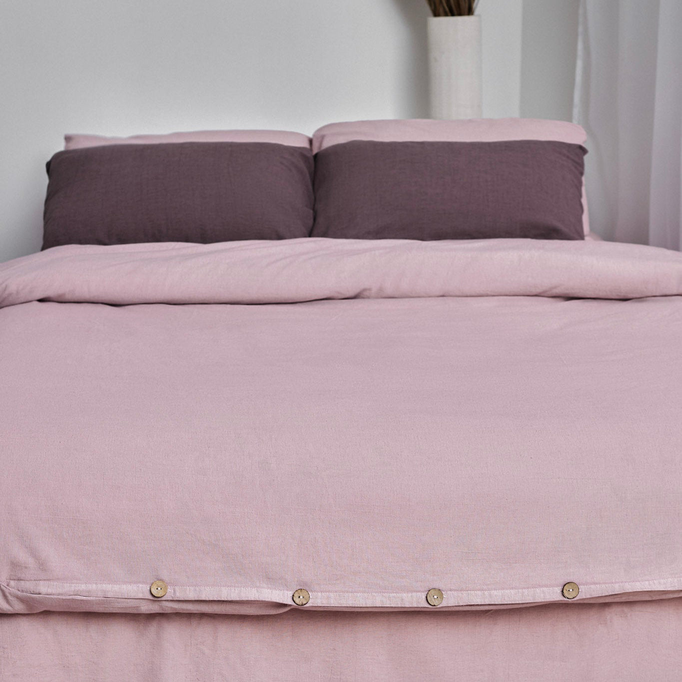 Pink linen duvet cover set with button details on a bed against a white wall.