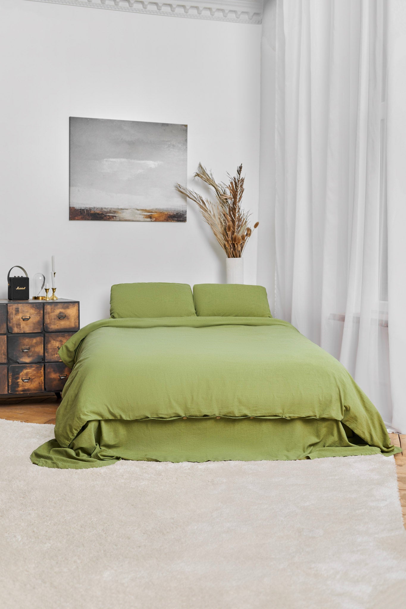 Bedroom with moss green linen bedding, wooden nightstand, and abstract painting on white wall. Modern classic design