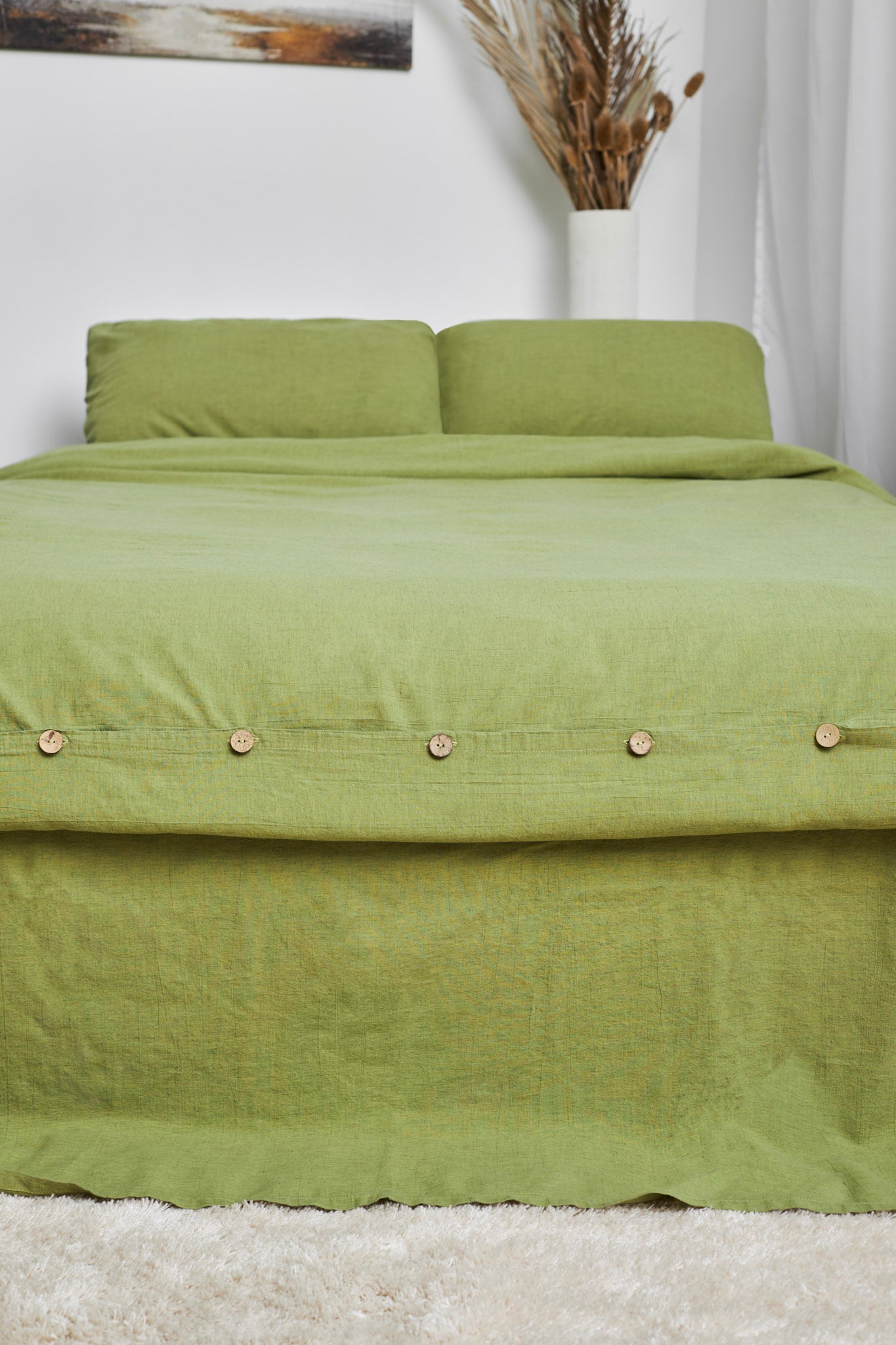 Green linen duvet cover set with button details on a bed against a white wall.