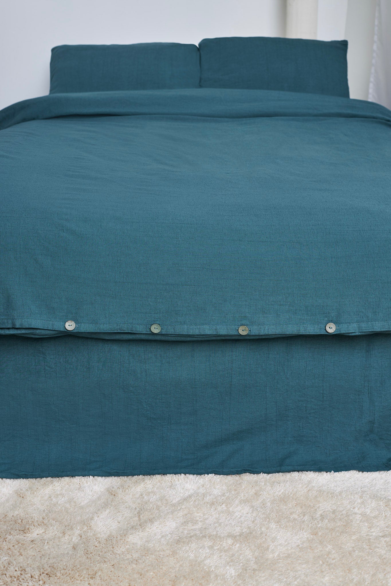 Teal linen duvet cover set on a bed with matching pillows against a white wall.
