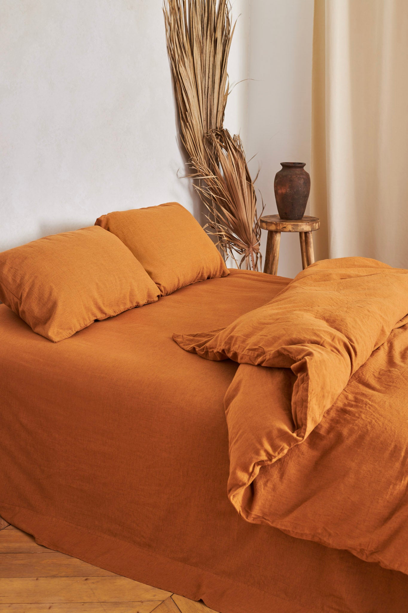 terracotta brown linen bedding set with matching pillows on a bed in a room with a vase and plant decor.
