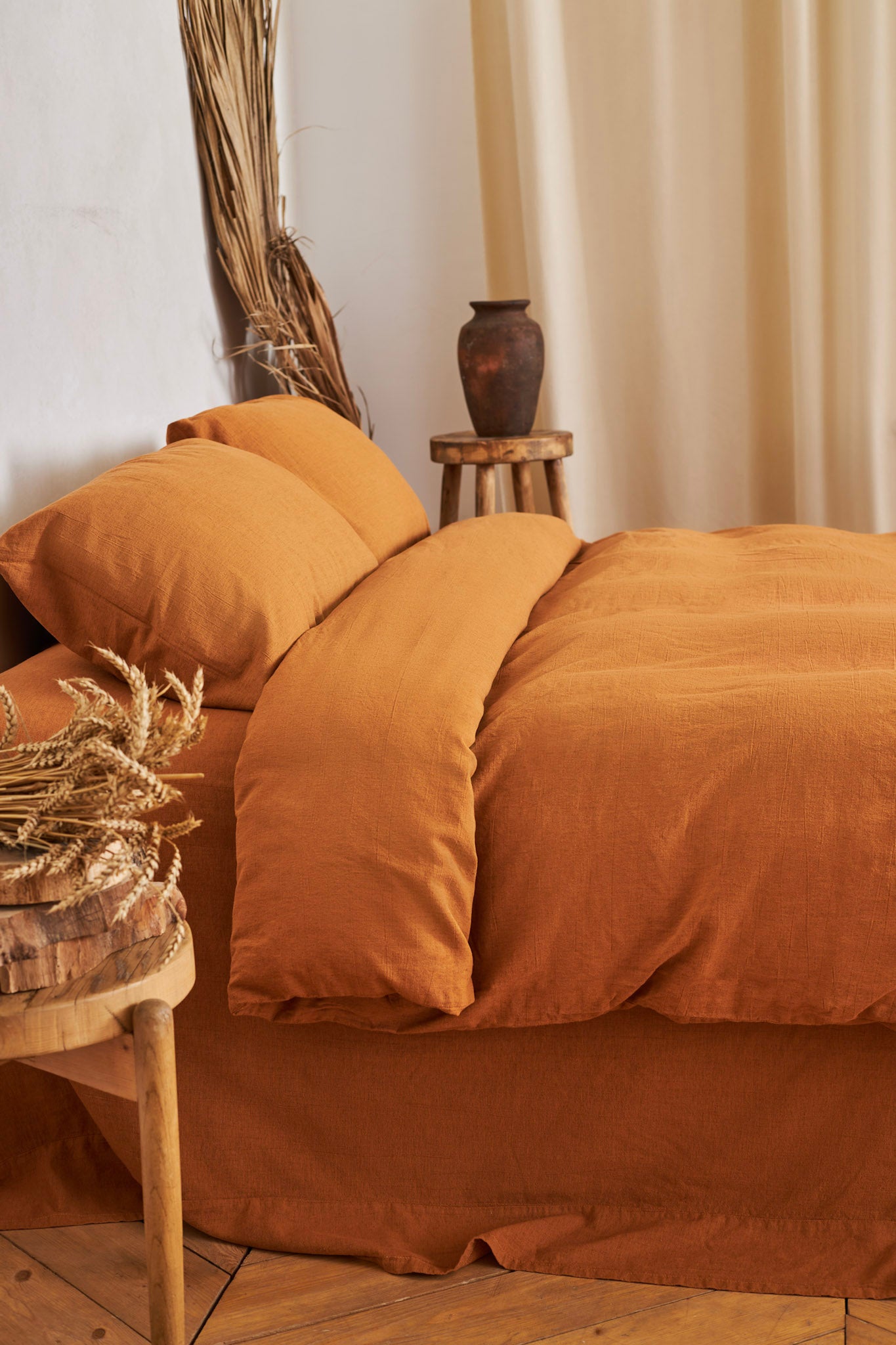 burnt orange linen bedding set on a bed with a wooden side table and decorative elements.