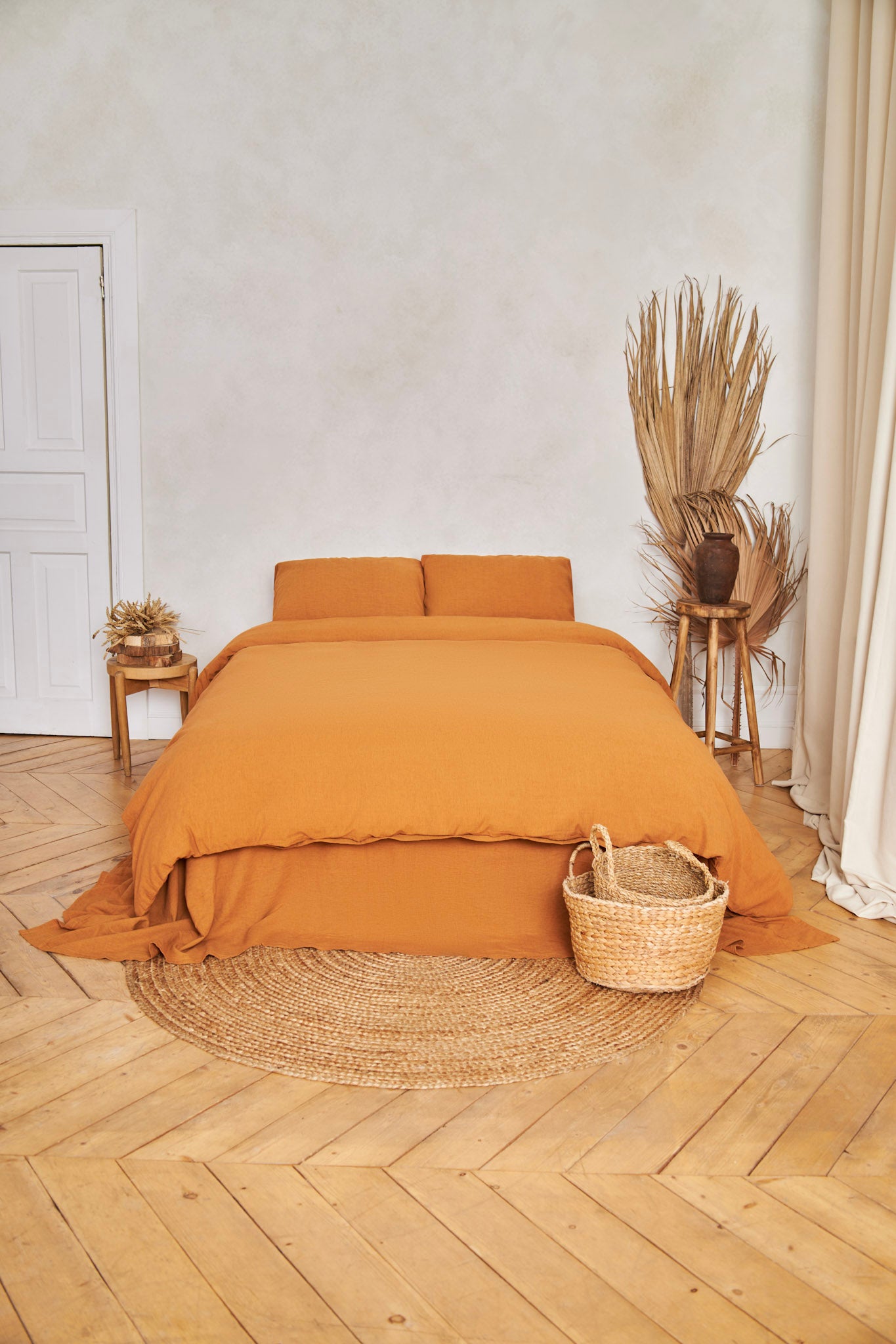 Bed with cinnamon-colored linen duvet cover set in a room with wooden flooring and decorative elements.