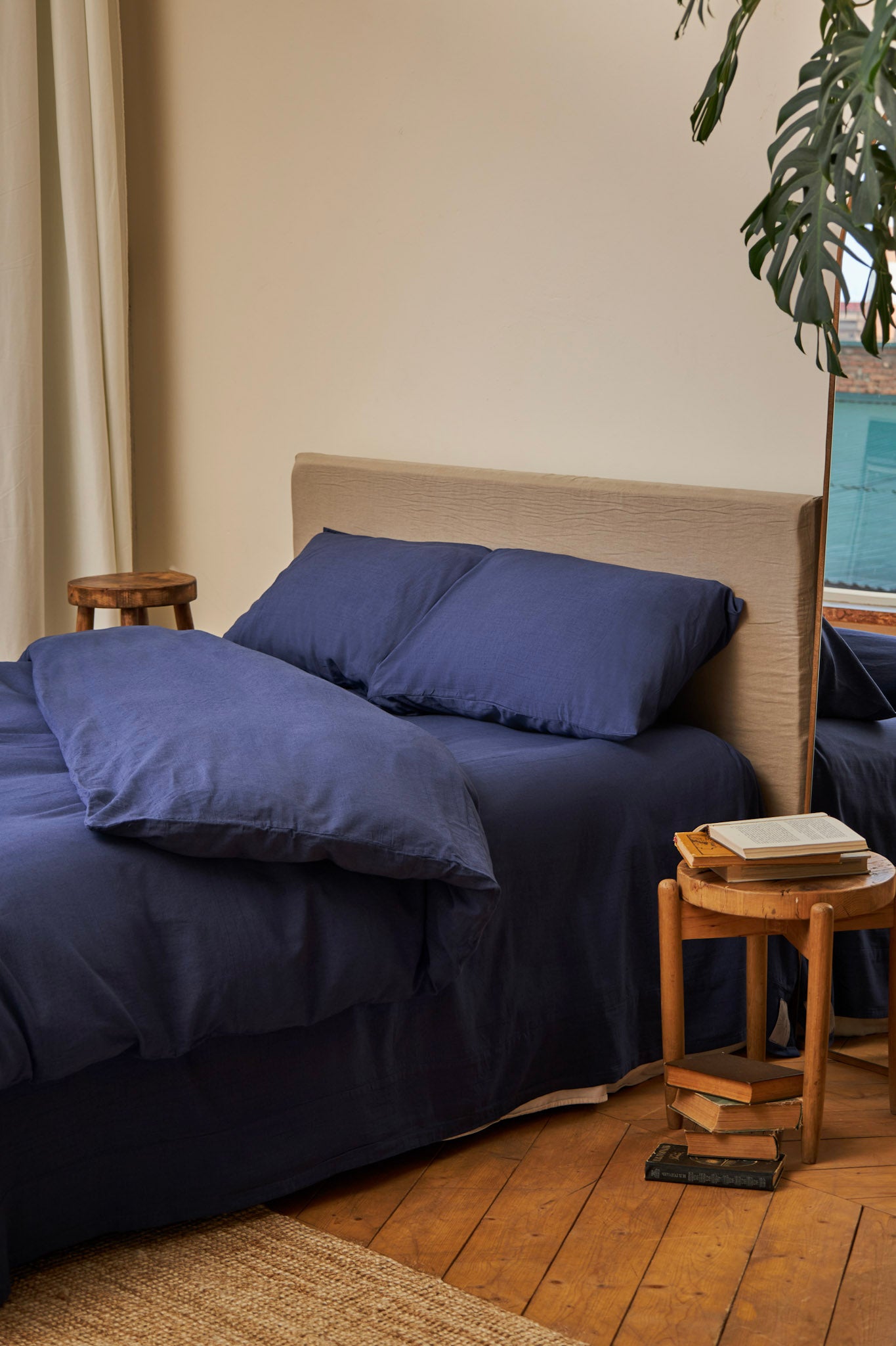 Navy blue linen bedding set stonewashed placed on a bed in a bedroom with wooden flooring and a plant.