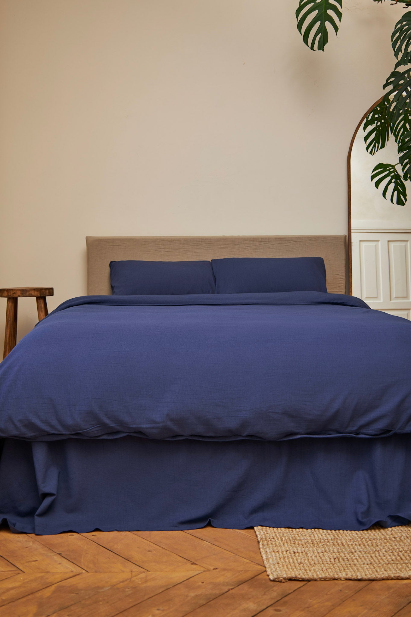 Navy blue linen bedding set on a bed in a room with wooden flooring and a plant.