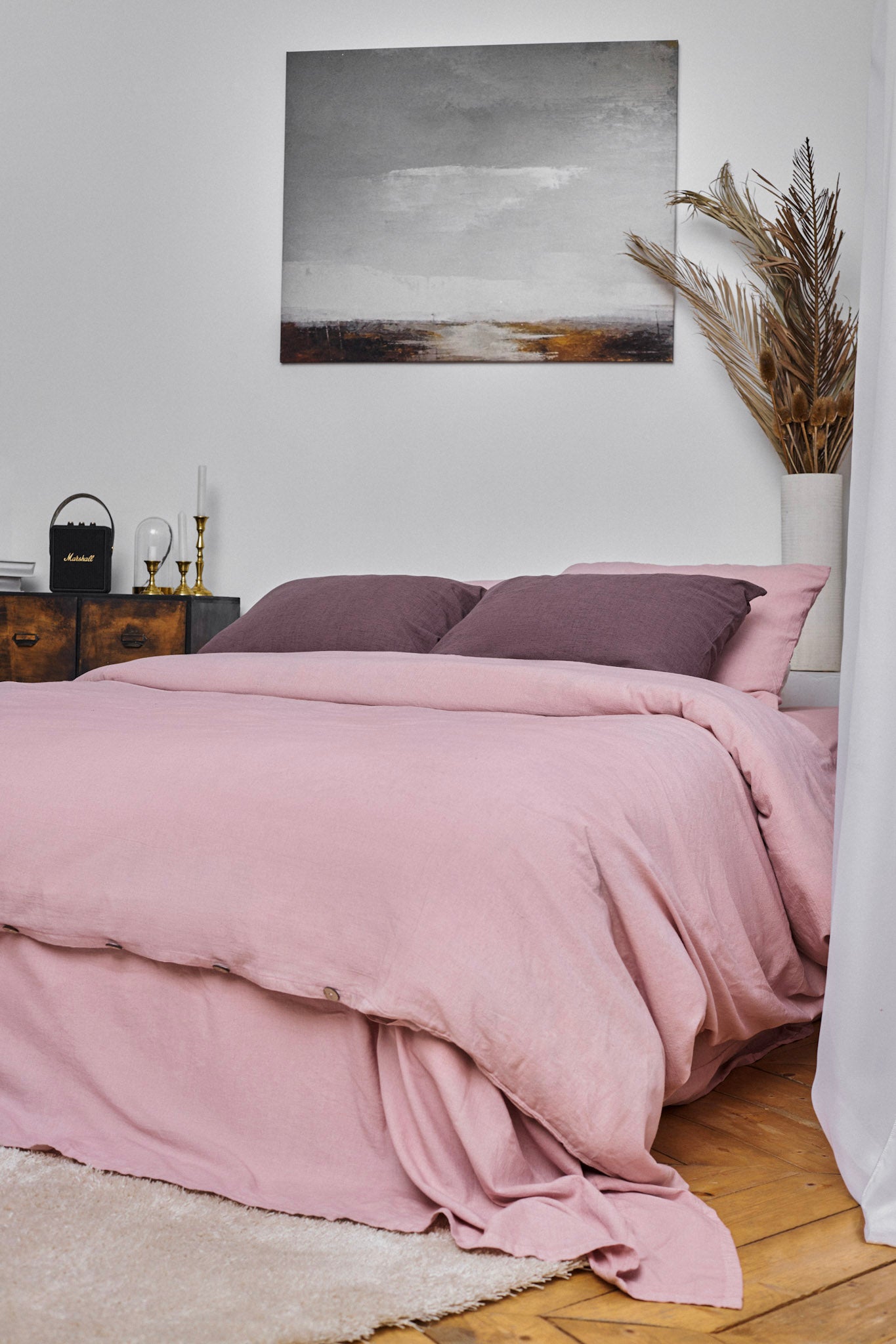 Bedroom with pink linen bedding - a linen duvet cover and linen pillowcases, purple linen pillows, and a painting on the wall.