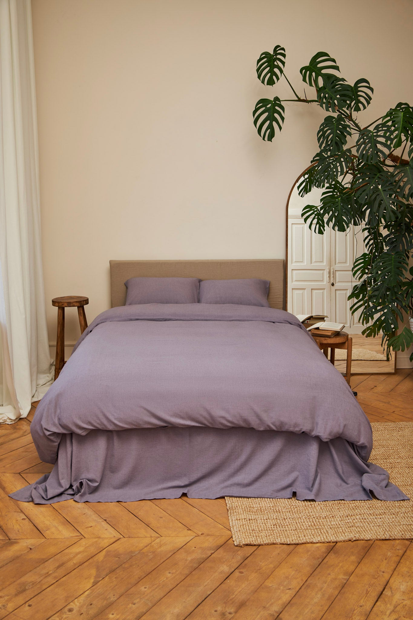 Purple lavender linen bedding set on a bed in a room with wooden flooring and a plant.