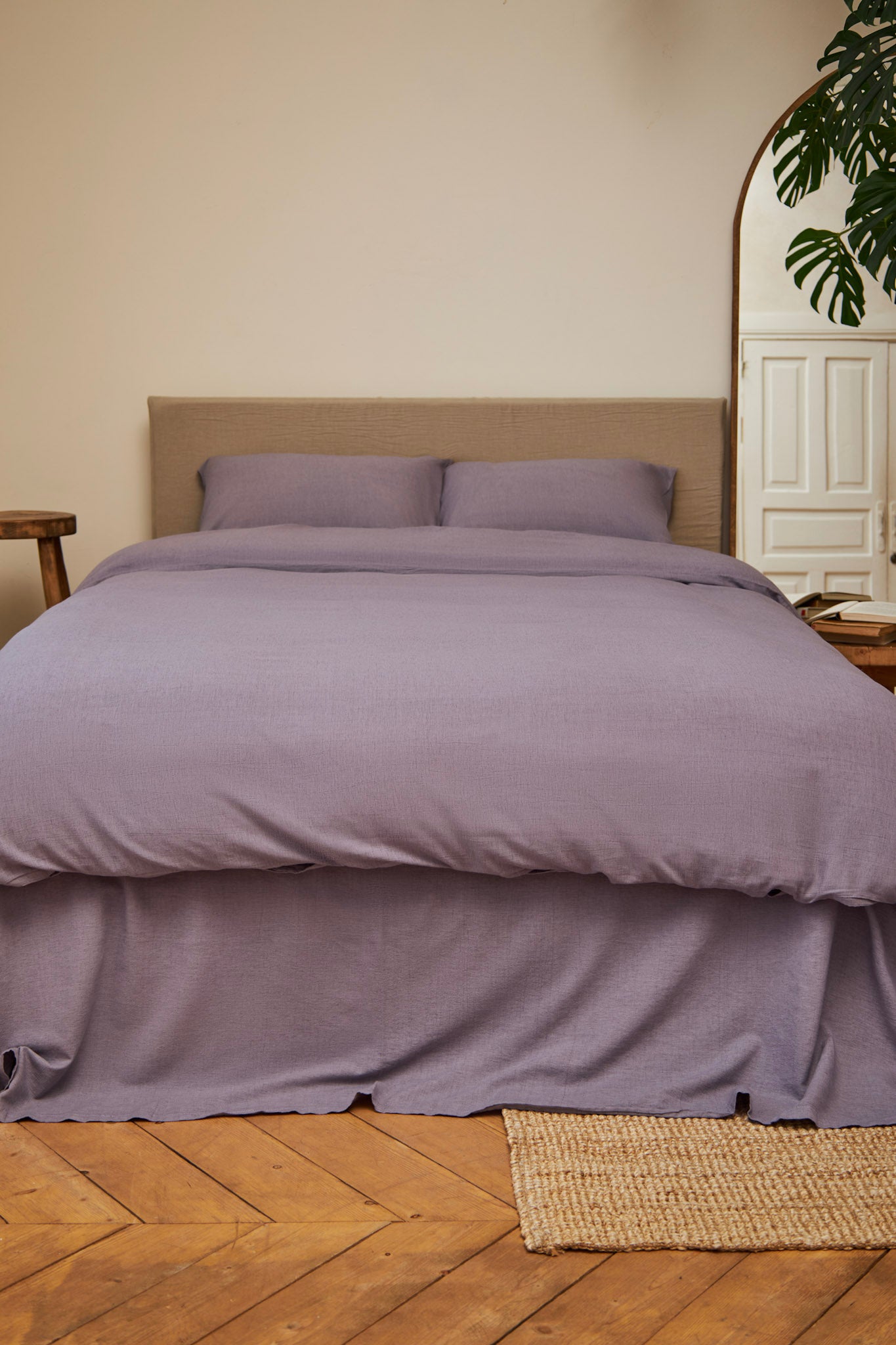 Lilac purple linen bedding set on a bed in a room with wooden flooring and a plant.