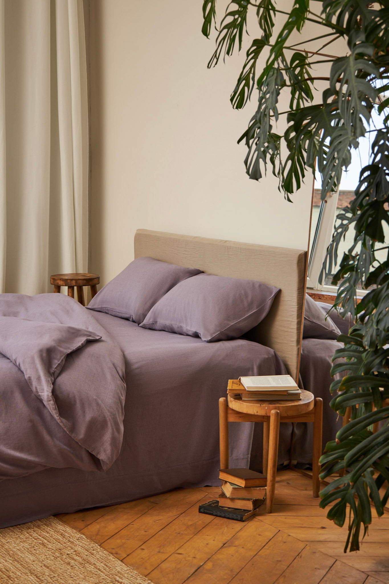 Classy bedroom with a duvet cover set in dusty purple color on a bed with side table and plants next to it 