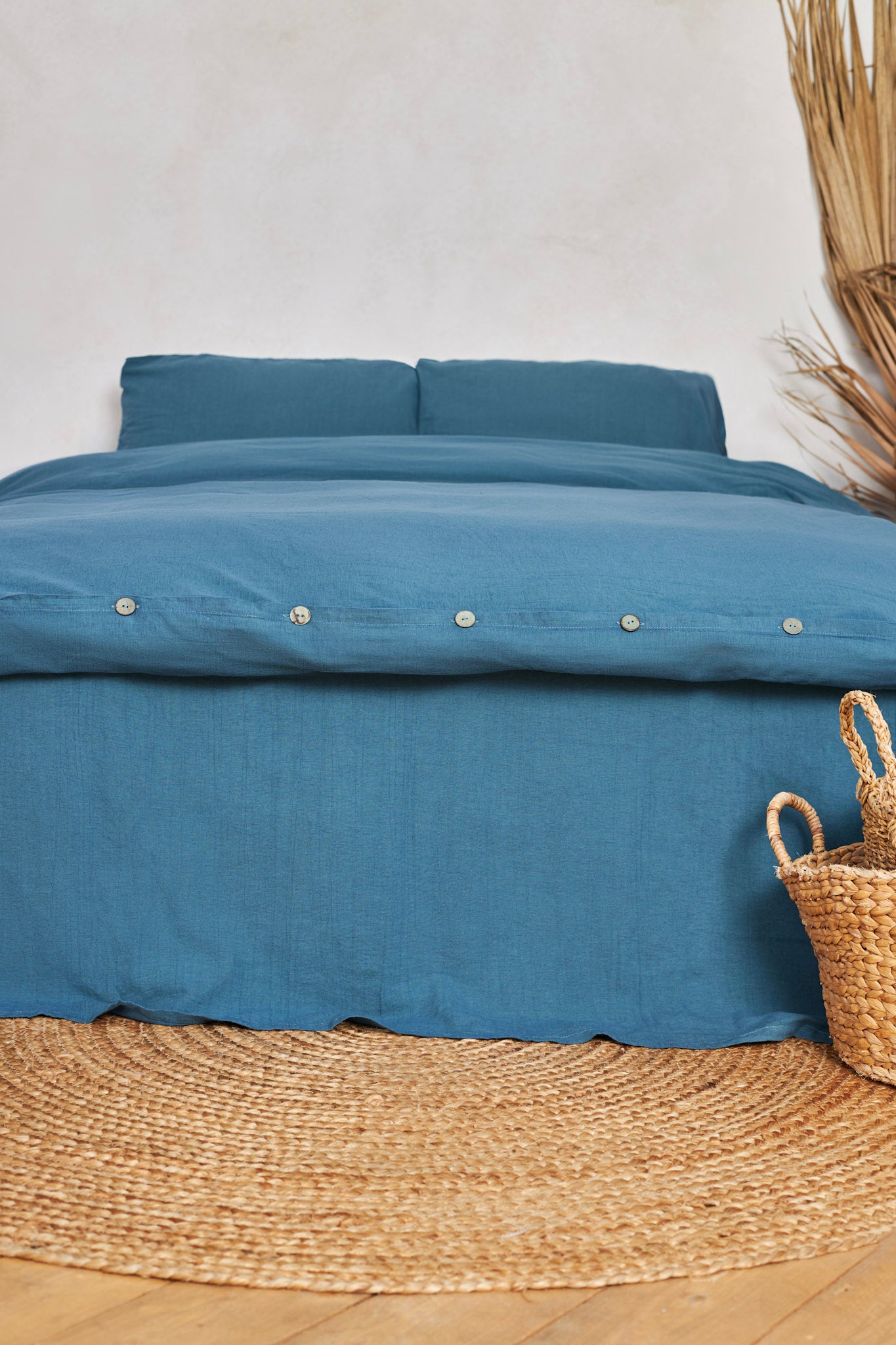 Blue stonewashed linen bedding set on a bed with a woven basket on a wooden floor.