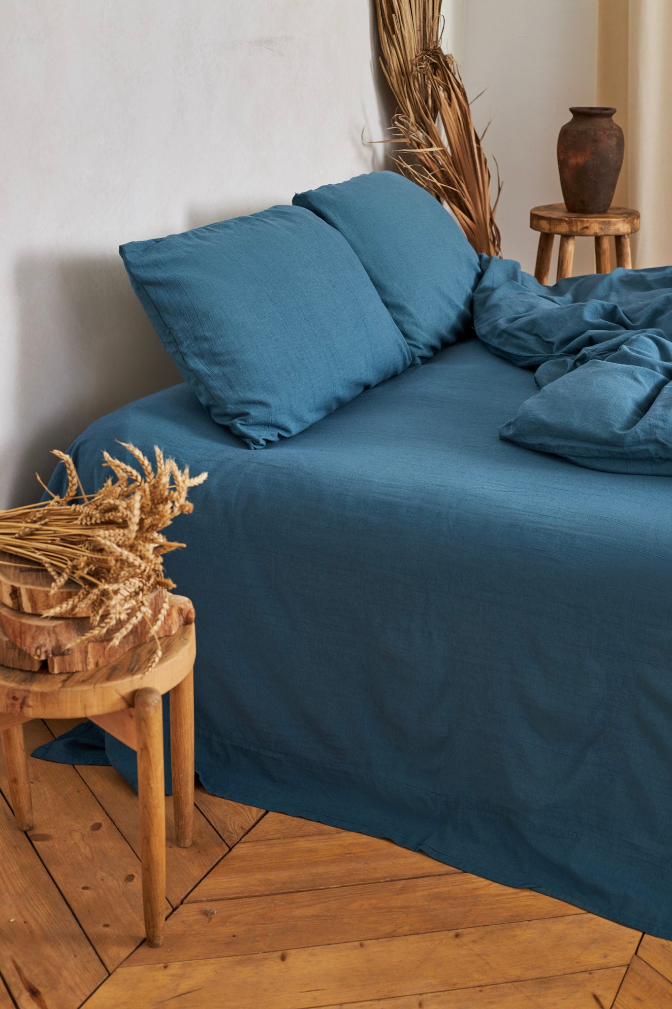 Blue linen duvet cover set on a bed with wooden stools and decorative items in a room.